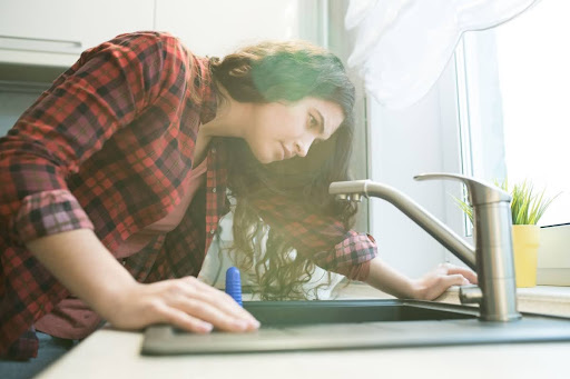 A woman inspecting a kitchen faucet.