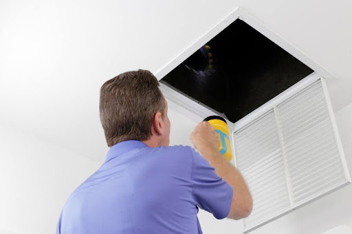 A man using a flashlight to inspect HVAC ductwork.